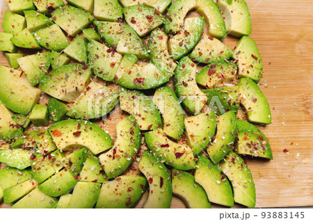 Top view Avocado slices on a wooden textured background sprinkled with spices, bright accent. View from above 93883145