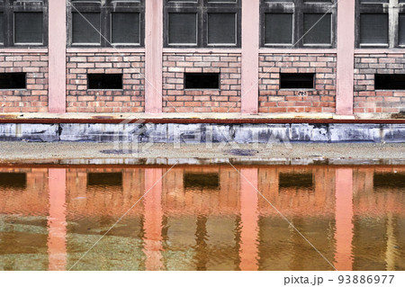 Dull monotonous industrial facade reflected in dirty water of a puddle 93886977