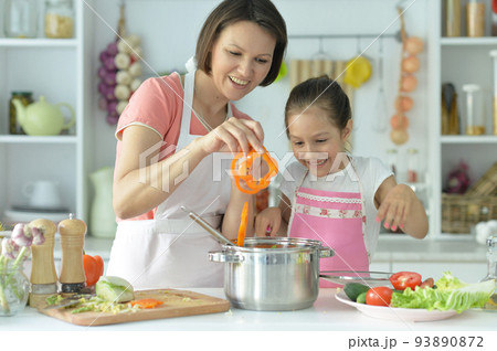 Cute little girl with her mother cooking together at kitchen table 93890872