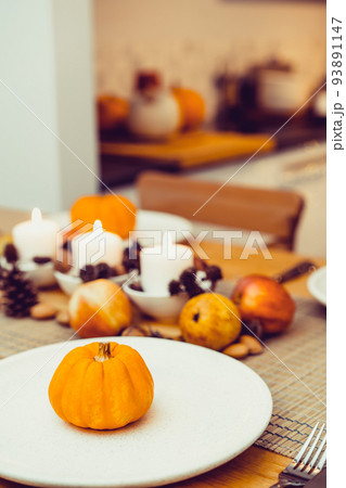Fall table setting for celebration Thanksgiving day family party. Autumn composition with candles, fruits, nuts and cones. Plates with pumpkins and pomegranate. Natural autumn decor. Selective focus Fall table setting for celebration Thanksgiving day family party. Autumn composition with candles, fruits, nuts and cones. Plates with pumpkins and pomegranate. Natural autumn decor. Selective focus 93891147