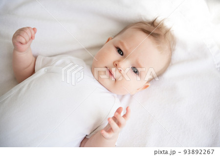 Charming baby on a white bed in the bedroom. Charming baby on a white bed in the bedroom. 93892267
