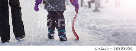 The girl is holding a red sled in her hands to ride the hill. Sledging. Activities for children and teenagers. Winter entertainment and sports. The girl is holding a red sled in her hands to ride the hill. Sledging. Activities for children and teenagers. Winter entertainment and sports. 93895050