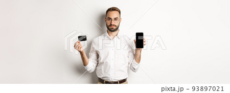 Serious business man showing mobile screen and credit card. Concept of online shopping Serious business man showing mobile screen and credit card. Concept of online shopping 93897021