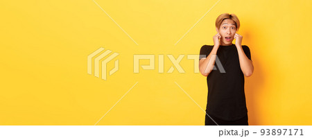 Excited handsome blond guy in black clothes, looking tempted and standing over yellow background Excited handsome blond guy in black clothes, looking tempted and standing over yellow background 93897171