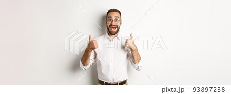 Excited man in glasses showing thumbs up and looking amazed, agree and approve something great, recommending product, standing over white background Excited man in glasses showing thumbs up and looking amazed, agree and approve something great, recommending product, standing over white background 93897238