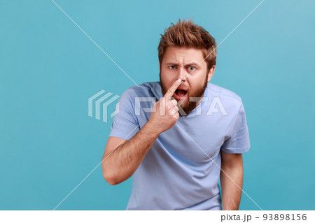 You are liar. Portrait of shocked bearded man standing, touching his nose and showing lie gesture, suspecting falsehood, dishonest talk. Indoor studio shot isolated on blue background. 93898156