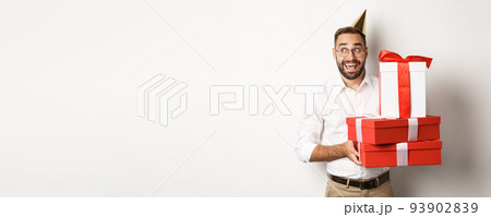 Holidays and celebration. Excited man having birthday party and receiving gifts, looking happy, standing over white background Holidays and celebration. Excited man having birthday party and receiving gifts, looking happy, standing over white background 93902839