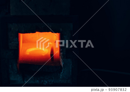 Blacksmith forge oven with hot flame. Smith heating iron of steel horseshoe in fire of red-hot forge. 93907832