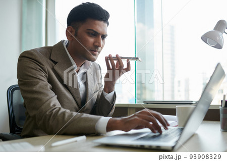 Serious Indian entrepreneur recording voice message for coworker when checking e-mails on laptop 93908329