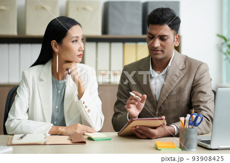 Young Indian entrepreneur asking assistant to correct some details in contract on tablet computer Young Indian entrepreneur asking assistant to correct some details in contract on tablet computer 93908425