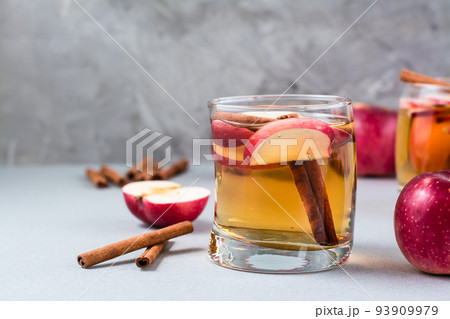 Fresh organic apple cider with cinnamon in glass and apples on a gray background. Warming winter drinks. Copy space Fresh organic apple cider with cinnamon in glass and apples on a gray background. Warming winter drinks. Copy space 93909979