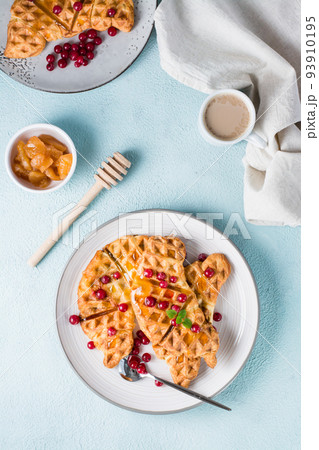 Crispy croffles with red currants, honey and mint on plates, a cup of coffee and jam on a light table. Sweet delicious breakfast. Vertical and top view 93910195
