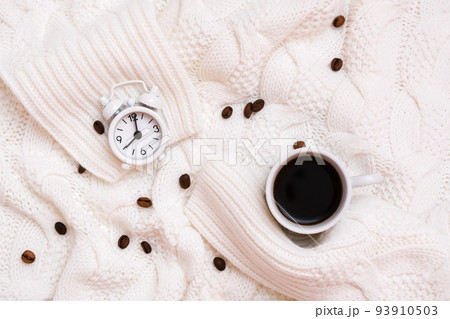 Cup of black coffee, alarm clock and coffee beans on a cozy white sweater. Time to drink coffee concept. Top view Cup of black coffee, alarm clock and coffee beans on a cozy white sweater. Time to drink coffee concept. Top view 93910503