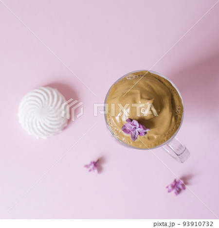 Beautiful dalgon coffee drink. Coffee mug with foam and lilac flower on a lilac pink background. Top view Beautiful dalgon coffee drink. Coffee mug with foam and lilac flower on a lilac pink background. Top view 93910732