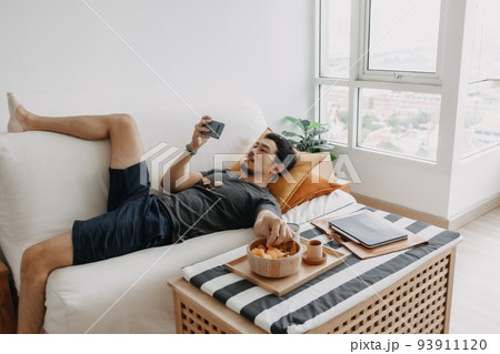 Man watch online tv and eating snack instead of working from home. 93911120