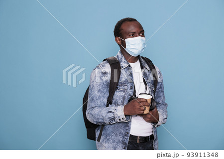 Man with DSLR device and protective mask wearing backpack while enjoying urban cityscape. Professional photographer wearing virus protection facemask and having camera while going on vacation trip. 93911348