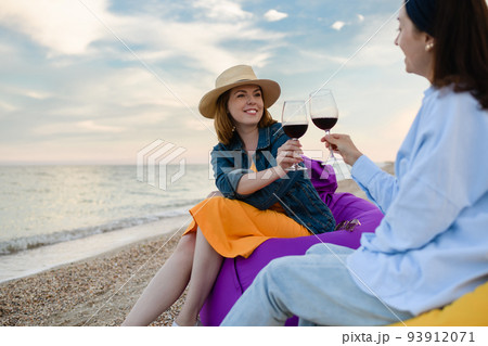 Two pretty young women with glasses of red wine by the sea. Two pretty young women with glasses of red wine by the sea. 93912071