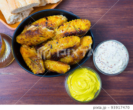 Dish of tasty fried chicken wings served in black bowl, two sauses 93917470