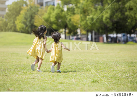 夏の芝生の公園で元気に遊ぶ姉妹 93918397