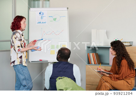 Young confident broker in casualwear pointing at whiteboard with graph Young confident broker in casualwear pointing at whiteboard with graph 93921204