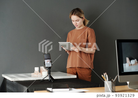 Young woman in casualwear using tablet while standing in front of workplace 93921329