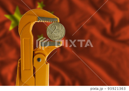 Russian two rubles coin held in an orange plumber wrench on the background of the flag of China. Reverse side of the coin. 93921363