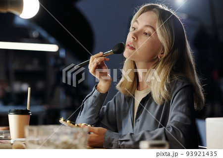 Young blond woman with cosmetic brush applying powder on her face Young blond woman with cosmetic brush applying powder on her face 93921435