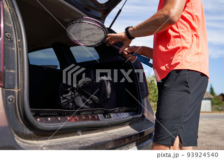 Sportsman getting bag and badminton rackets out of trunk outdoors 93924540