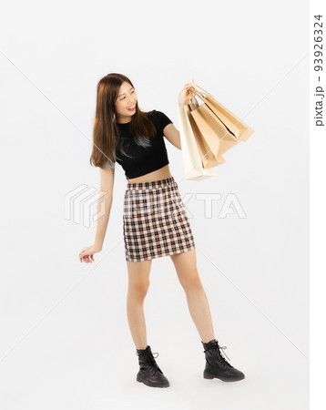 Young asian woman in black crop top t-shirt striped skirt and ankle boots carrying brown paper shopping bags on white background, full body. Young asian woman in black crop top t-shirt striped skirt and ankle boots carrying brown paper shopping bags on white background, full body. 93926324