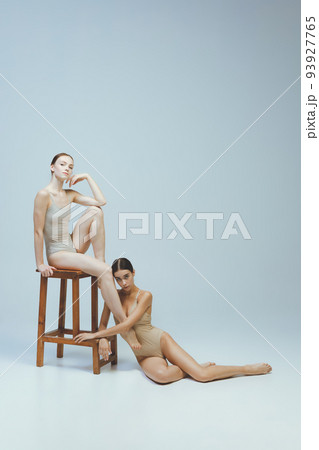 Portrait of beautiful, tender, young girl in beige bodysuits posing together isolated over grey studio background. Ballet 93927765