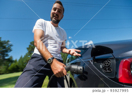 Caucasian man connect charger to electric car.  93927995