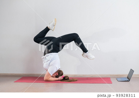A chubby young woman watches an online yoga lesson on a laptop. Distance sports training. Forearm stand 93928311