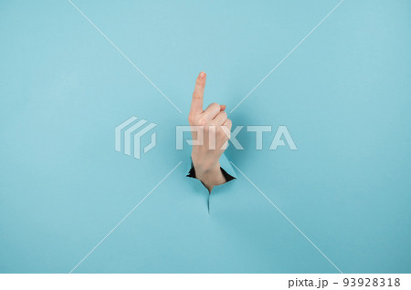 A woman's hand sticking out of a hole from a blue background shows her index finger up. 93928318