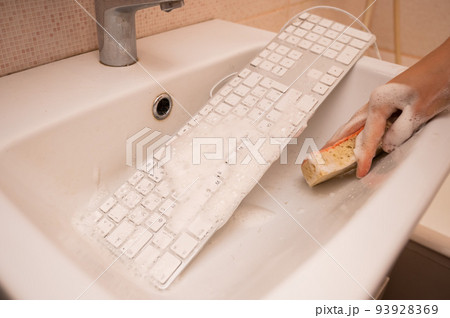 Woman washing white computer keyboard with a sponge with foam. Woman washing white computer keyboard with a sponge with foam. 93928369
