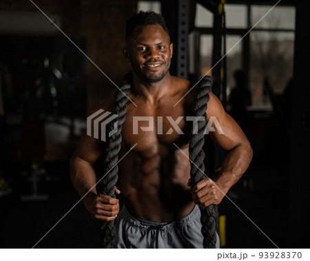 Muscular african american man posing with rope in gym.  93928370
