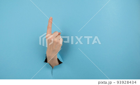 A woman's hand sticking out of a hole from a blue background shows her index finger up. 93928434
