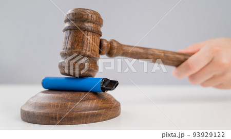 Judge hammering disposable vape with referee's gavel on white table. Judge hammering disposable vape with referee's gavel on white table. 93929122