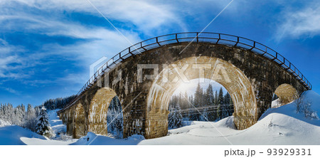 Stone viaduct (arch bridge) on railway through mountain snowy fir forest. Snow drifts on wayside and hoarfrost on trees. Stone viaduct (arch bridge) on railway through mountain snowy fir forest. Snow drifts on wayside and hoarfrost on trees. 93929331
