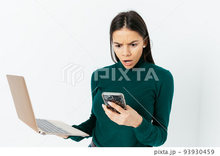 Shocked young woman looks at her smartphone in stress Shocked young woman looks at her smartphone in stress 93930459