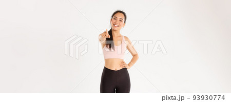 Sport, wellbeing and active lifestyle concept. Portrait of cheerful and enthusastic asian female fitness intrusctor, gym member in activewear inviting for training, pointing at camera and smiling 93930774
