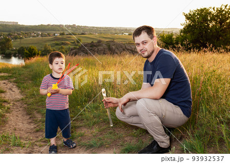 Dad and son play fun soap bubbles in nature in a yellow summer field. Hanging with his father, fatherhood and childhood. 93932537