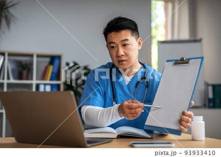 Serious mature asian man doctor show tablet to laptop in clinic office interior. Video call, treatment with therapist Serious mature asian man doctor show tablet to laptop in clinic office interior. Video call, treatment with therapist 93933410