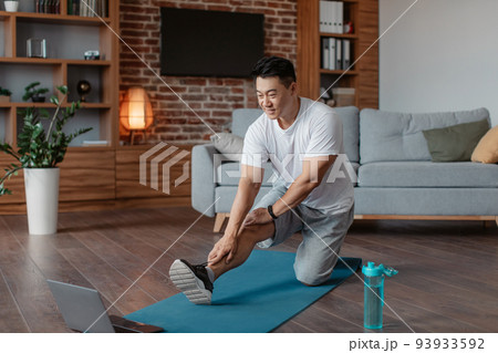 Active asian mature man in sportswear stretching leg muscles in front of laptop, watching online tutorials Active asian mature man in sportswear stretching leg muscles in front of laptop, watching online tutorials 93933592