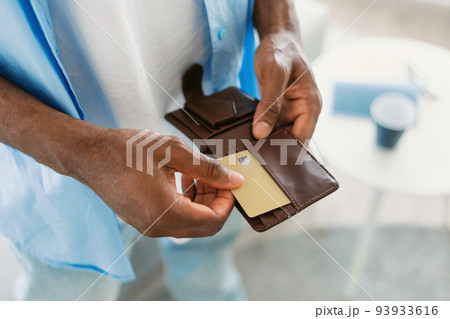 Unrecognizable black guy taking out credit card from his wallet, standing at home, closeup, copy space 93933616