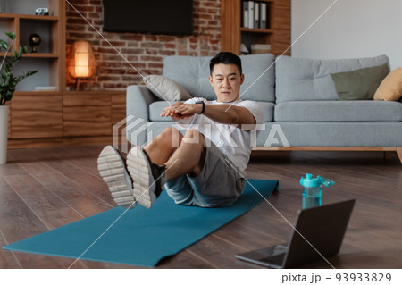 Mature korean man doing exercises for abs on mat on floor in living room interior, watching workout on laptop computer Mature korean man doing exercises for abs on mat on floor in living room interior, watching workout on laptop computer 93933829