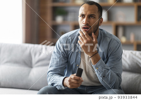 Shocked Black Man With Remote Controller In Hand Sitting On Couch 93933844