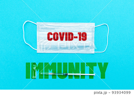 Medical protective mask, syringe and ampoule with vaccine on a blue background. Flat lay. Text immunity and covid-19. The concept of vaccination and new normal 93934099