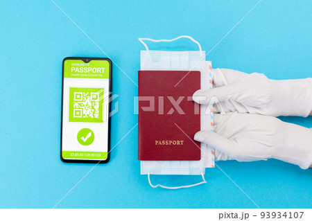 Hands in protective gloves give a passport with mask. Cellphone screen with an electronic health passport with qr-code. Flat lay. Concept of Covid-19 test for travel Hands in protective gloves give a passport with mask. Cellphone screen with an electronic health passport with qr-code. Flat lay. Concept of Covid-19 test for travel 93934107