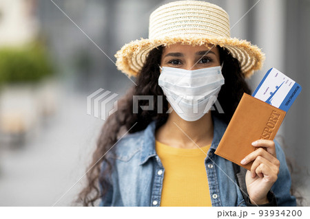 Closeup of woman in face mask holding passport and tickets Closeup of woman in face mask holding passport and tickets 93934200