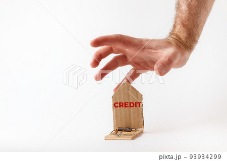 Bank investments and risks. a man's hand reaches for a mousetrap with a cardboard schematic house, with the inscription CREDIT. Copy space Bank investments and risks. a man's hand reaches for a mousetrap with a cardboard schematic house, with the inscription CREDIT. Copy space 93934299